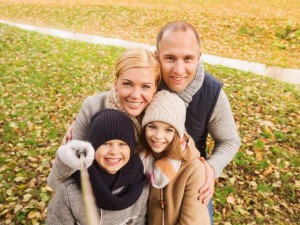 family, childhood, season, technology and people concept - happy family photographing with selfie stick in autumn park